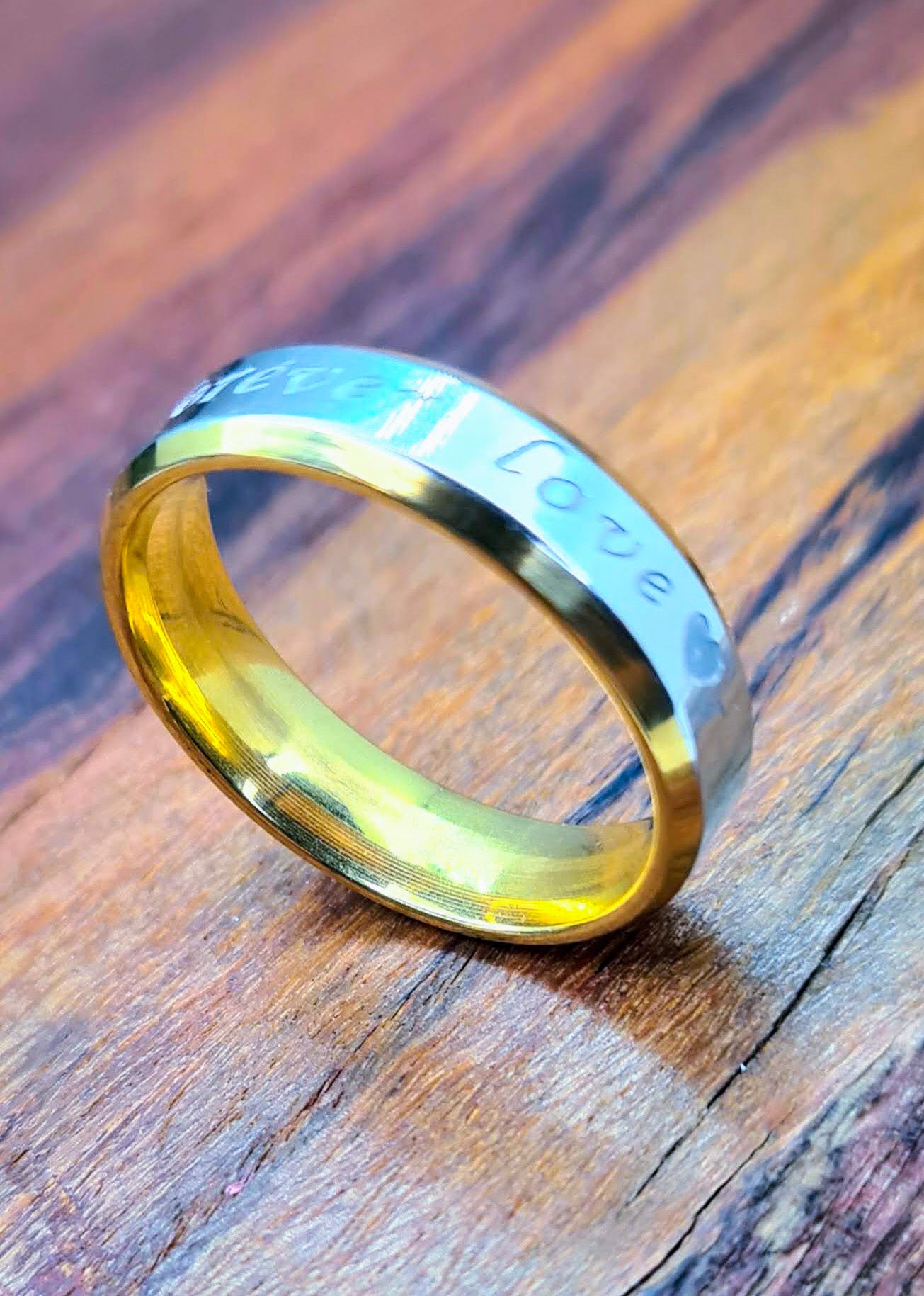 Anillo "Forever Love" tipo alianza de matrimonio o pareja en acero inoxidable bicolor y ancho de 6mm. Se incluye grabado de nombres y fecha importante gratis. Posa sobre madera.