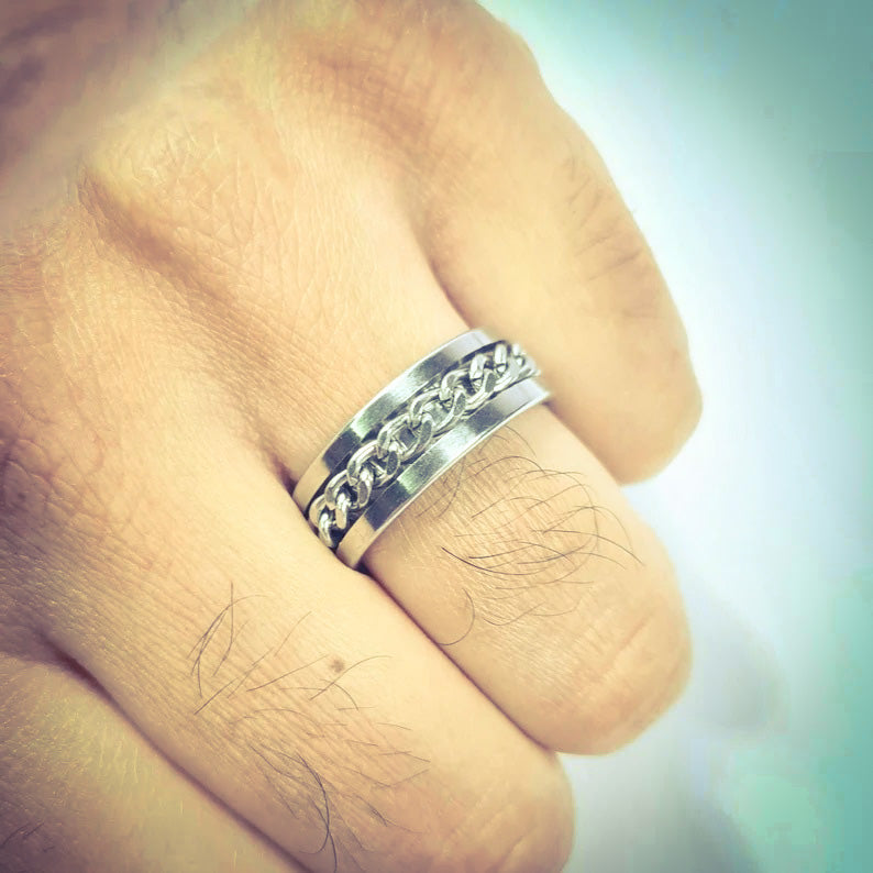 Anillo tipo alianza de matrimonio o pareja en acero inoxidable con cadena y ancho de 8mm. Se incluye grabado de nombres y fecha importante gratis. Posa sobre mano de hombre.
