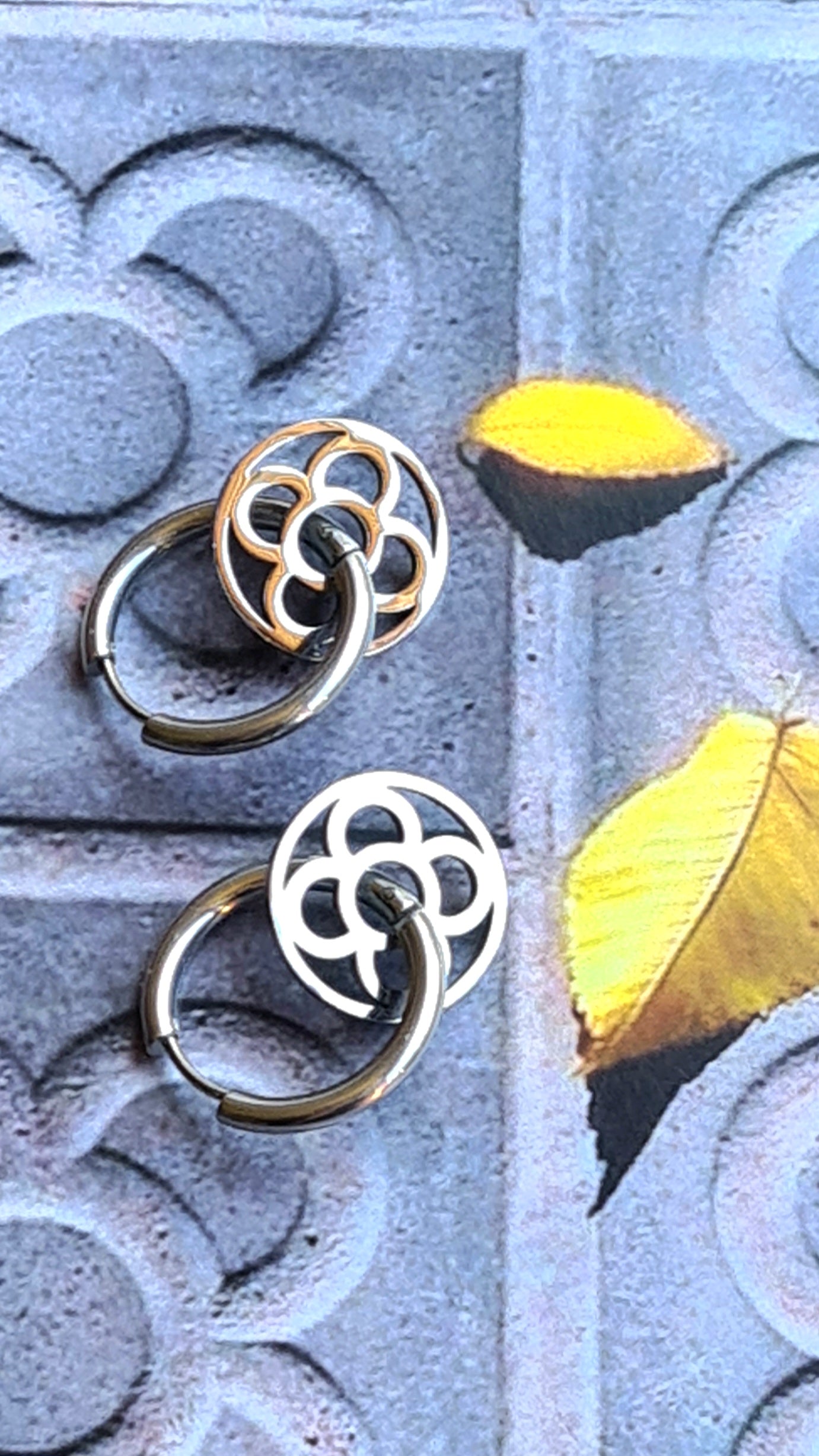 Aros con la Flor de Barcelona de acero inoxidable circular para mujer. Sobre baldosa Flor de Barcelona.