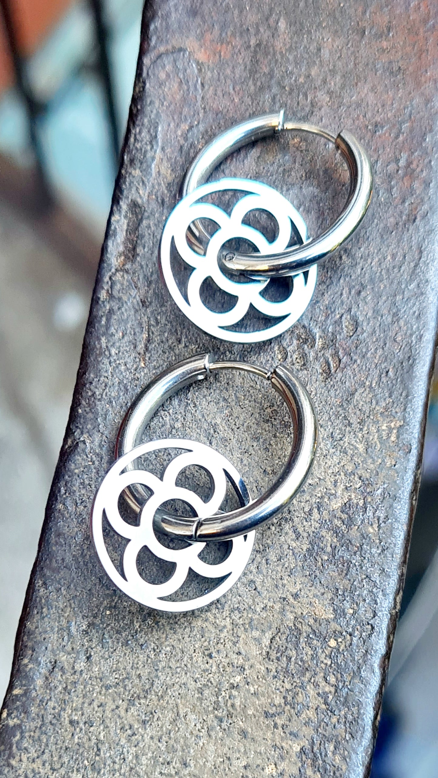 Aros con la Flor de Barcelona de acero inoxidable circular para mujer. Sobre baranda de hierro.
