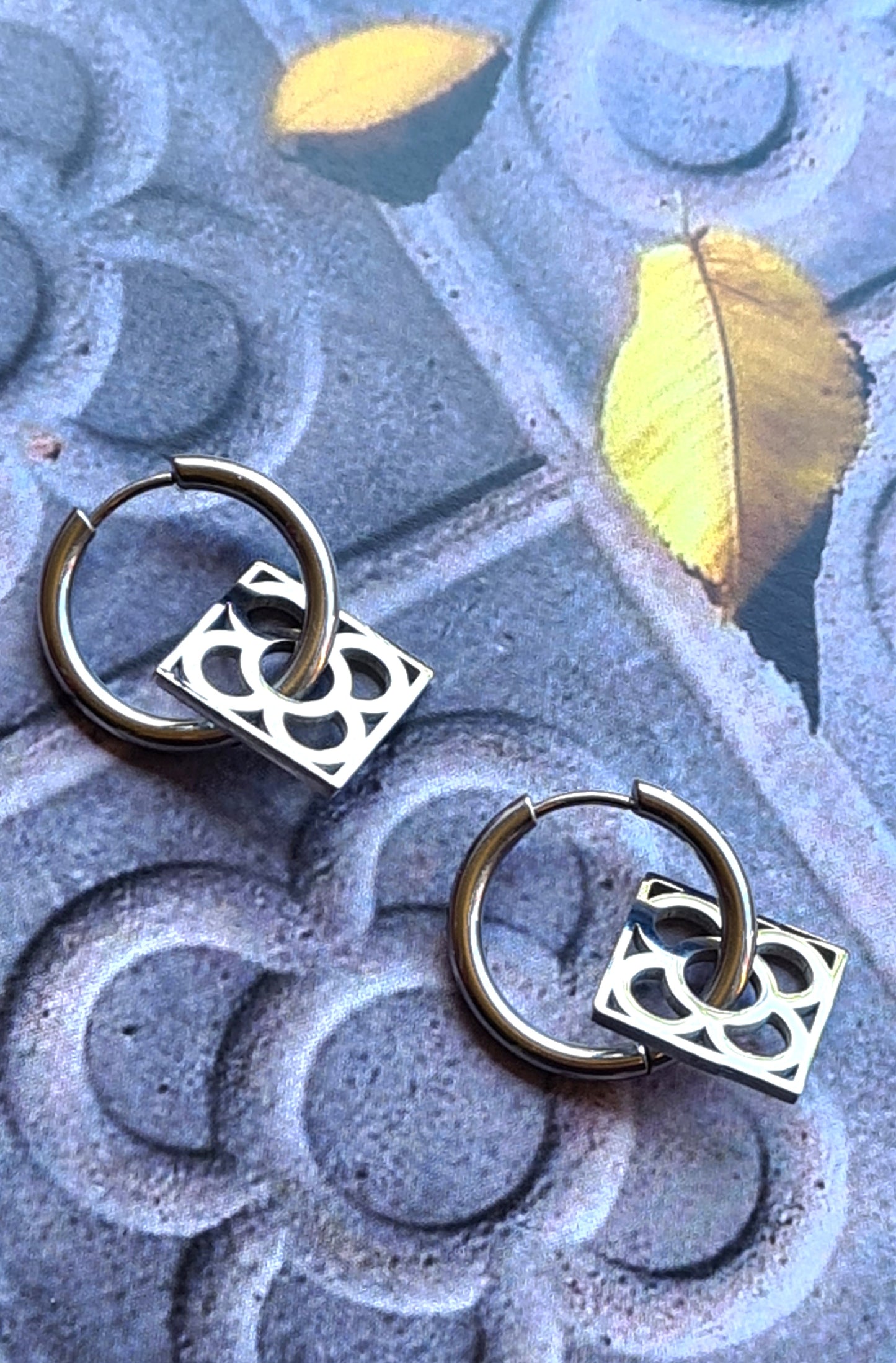 Aros con la Flor de Barcelona de acero inoxidable cuadrada para mujer. Sobre baldosa Flor de Barcelona.