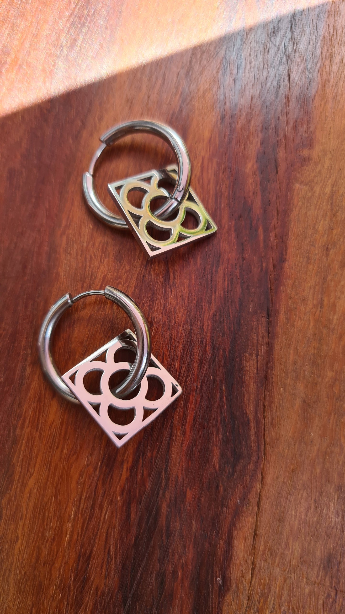 Aros con la Flor de Barcelona de acero inoxidable cuadrada para mujer. Fondo de Madera.