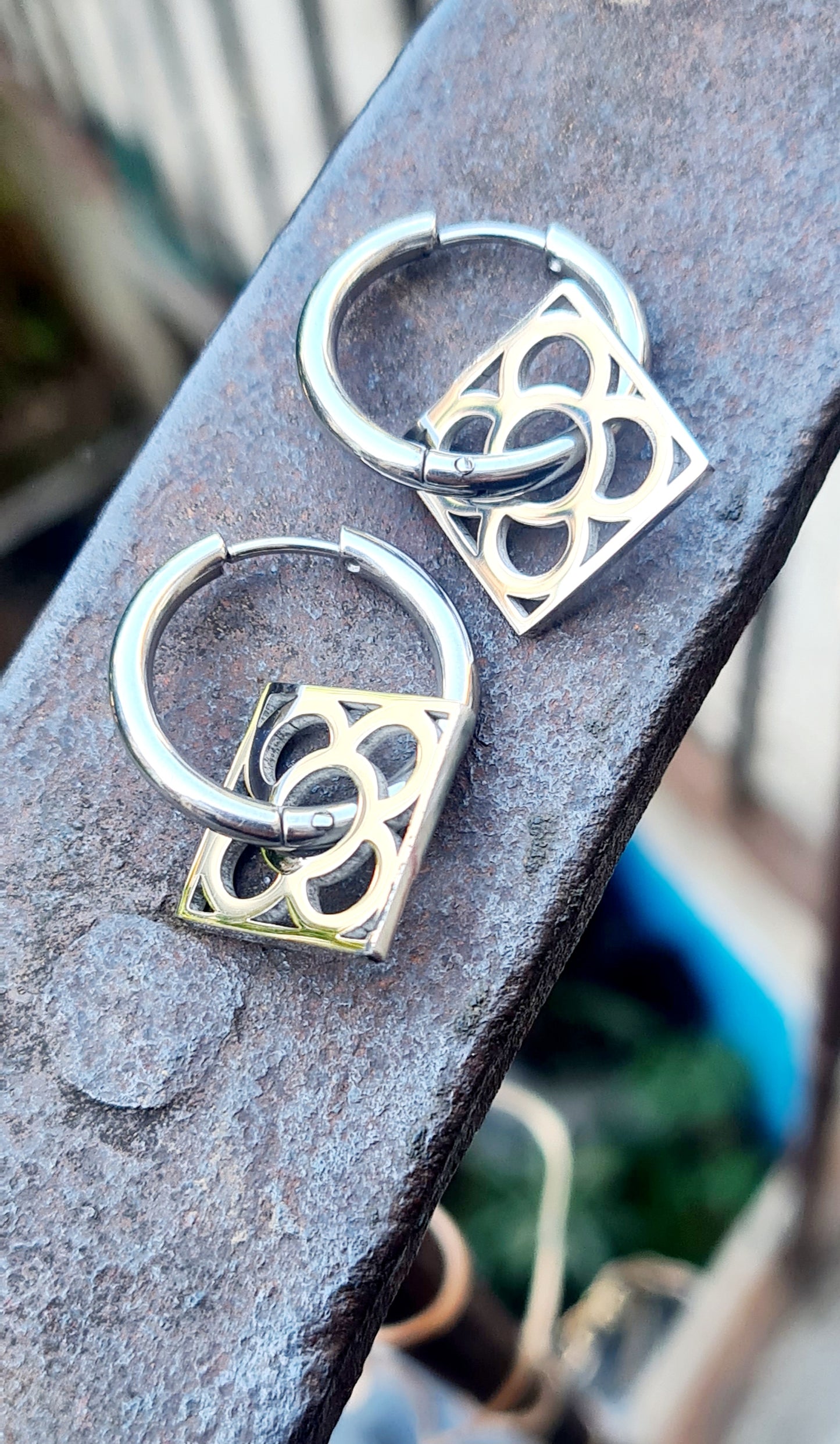 Aros con la Flor de Barcelona de acero inoxidable cuadrada para mujer. Sobre baranda de hierro.