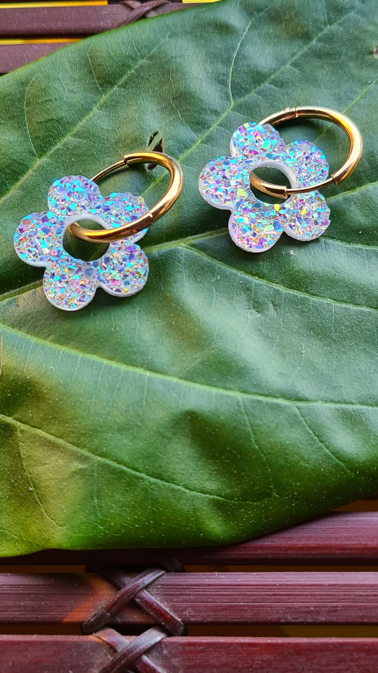 Aros acero inoxidable dorados con Flor de Acrílico Brillante para mujer. Fondo hoja verde.