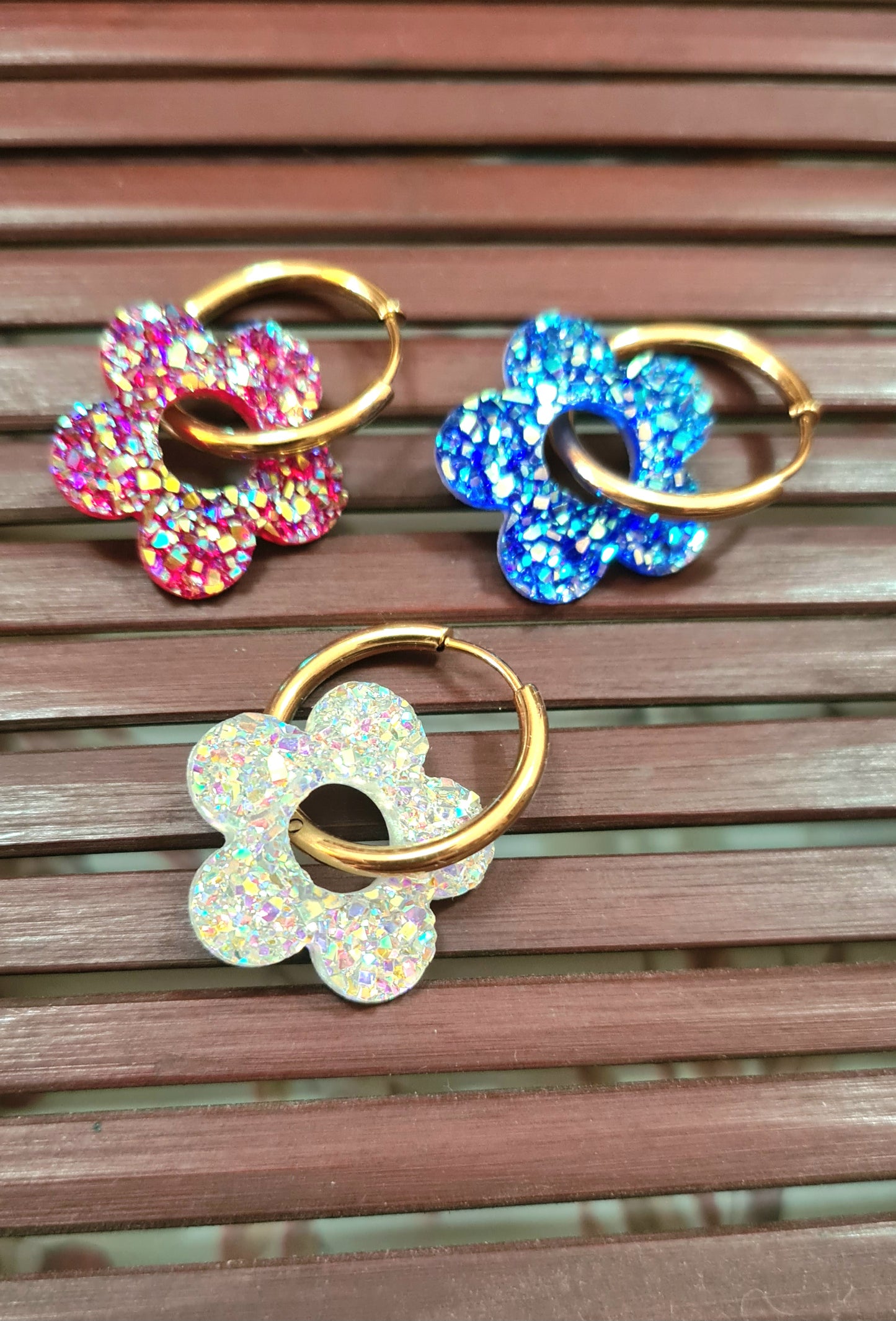 Aros acero inoxidable dorados con Flor de Acrílico Brillante para mujer. Fondo rejilla de Madera.