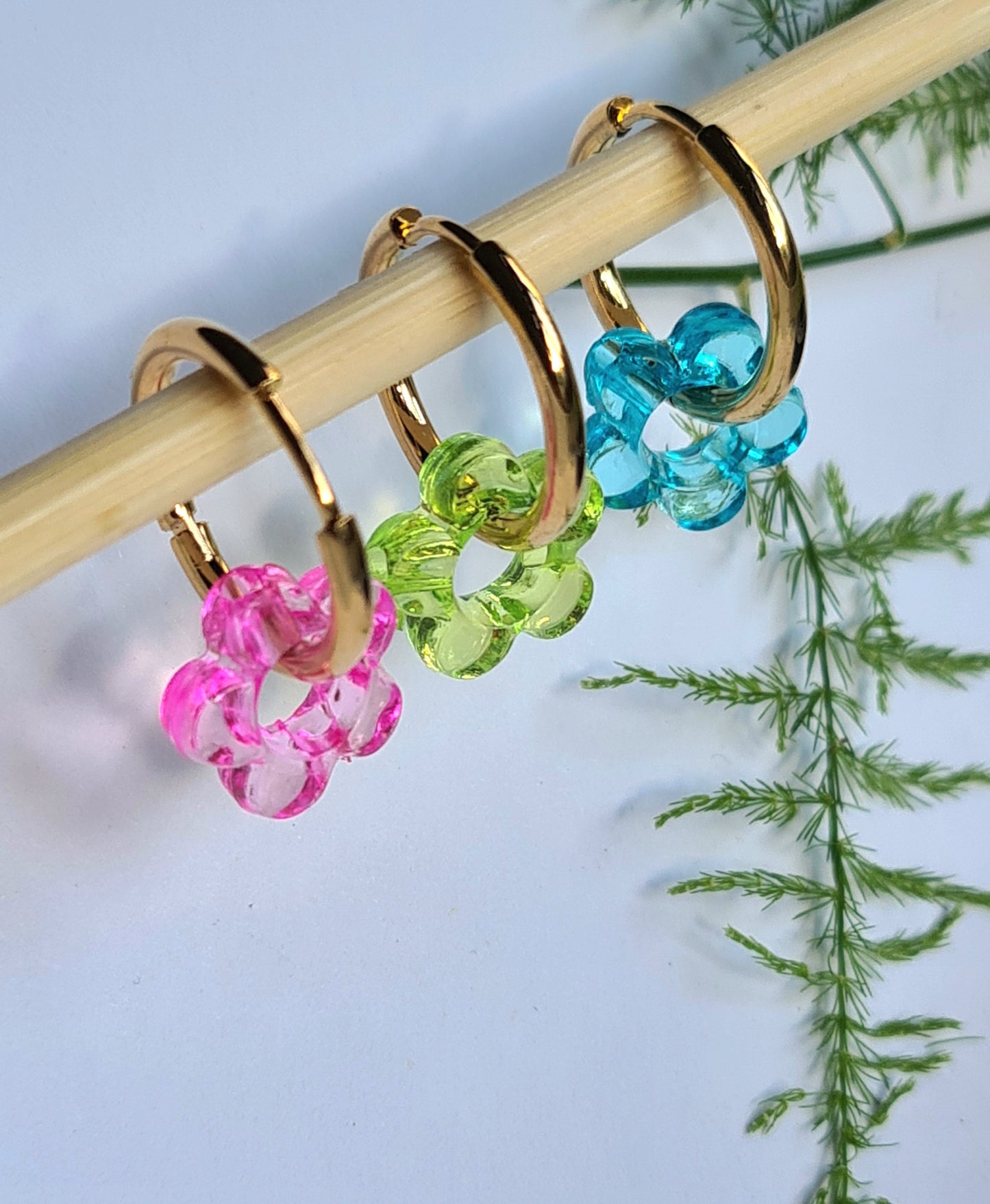 Aros acero inoxidable dorados con Flor de Acrílico para mujer. Fondo blanco con ramita.