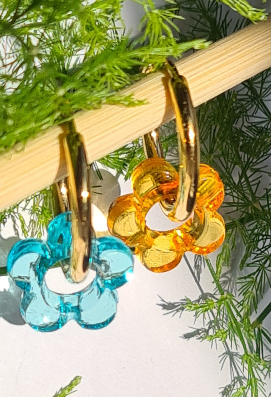 Aros acero inoxidable dorados con Flor de Acrílico para mujer. Fondo blanco con ramita.