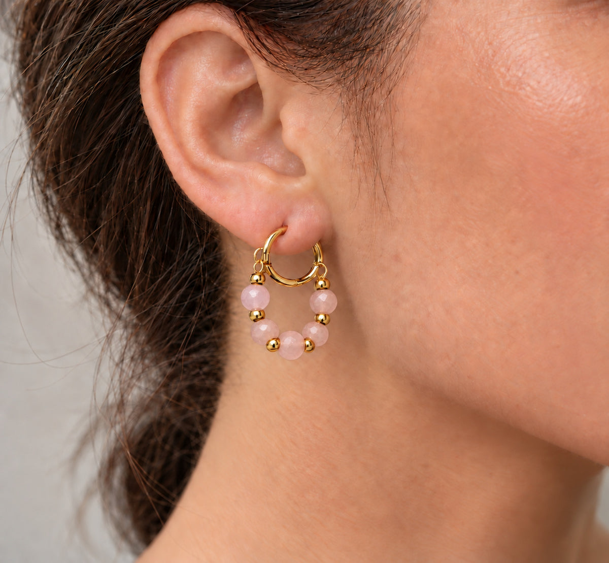Aro dorado con cuentas de cuarzo rosa llevado en la oreja.