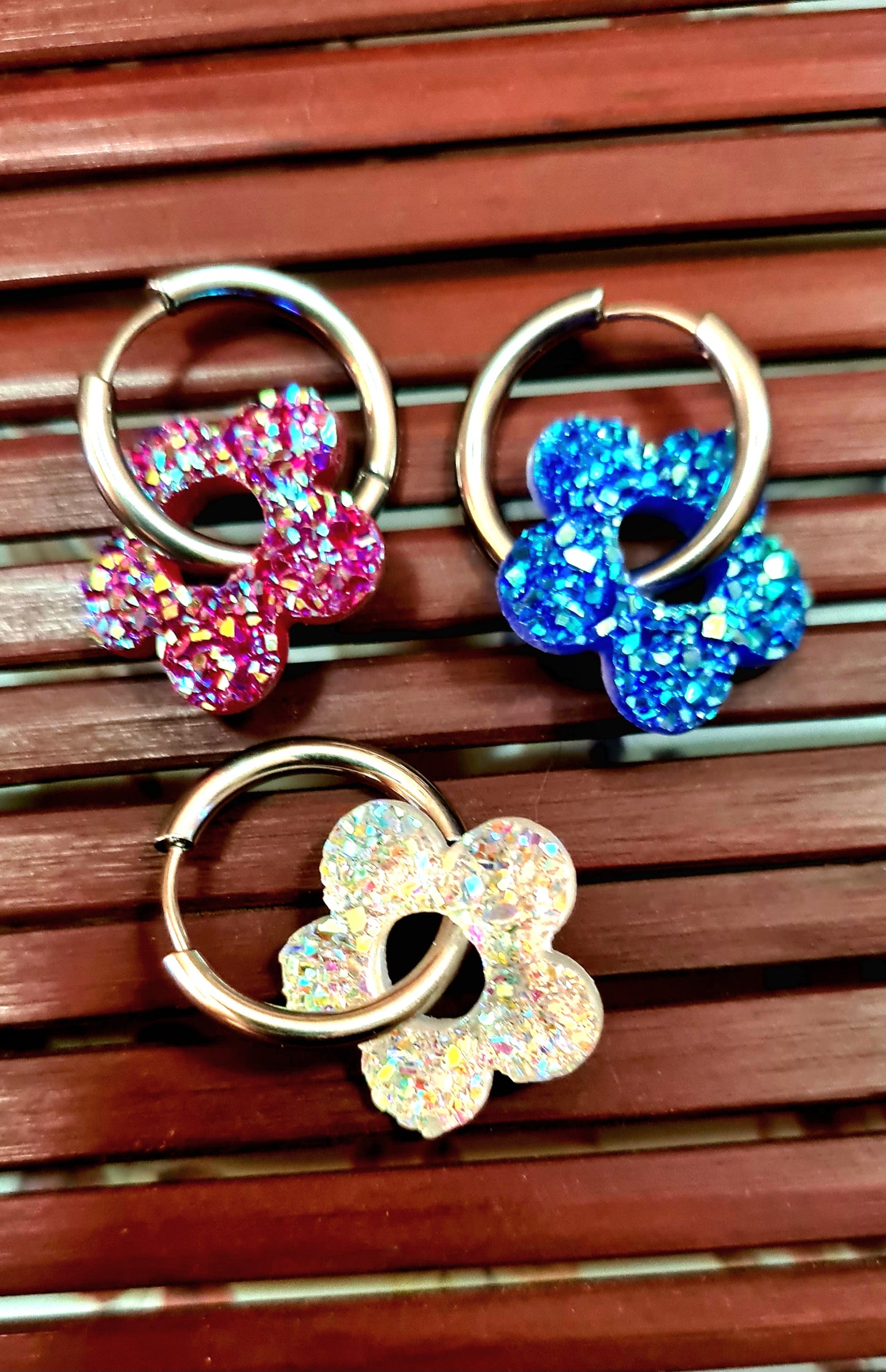 Aros acero inoxidable plateados con Flor de Acrílico Brillante para mujer. Fondo rejilla de Madera.