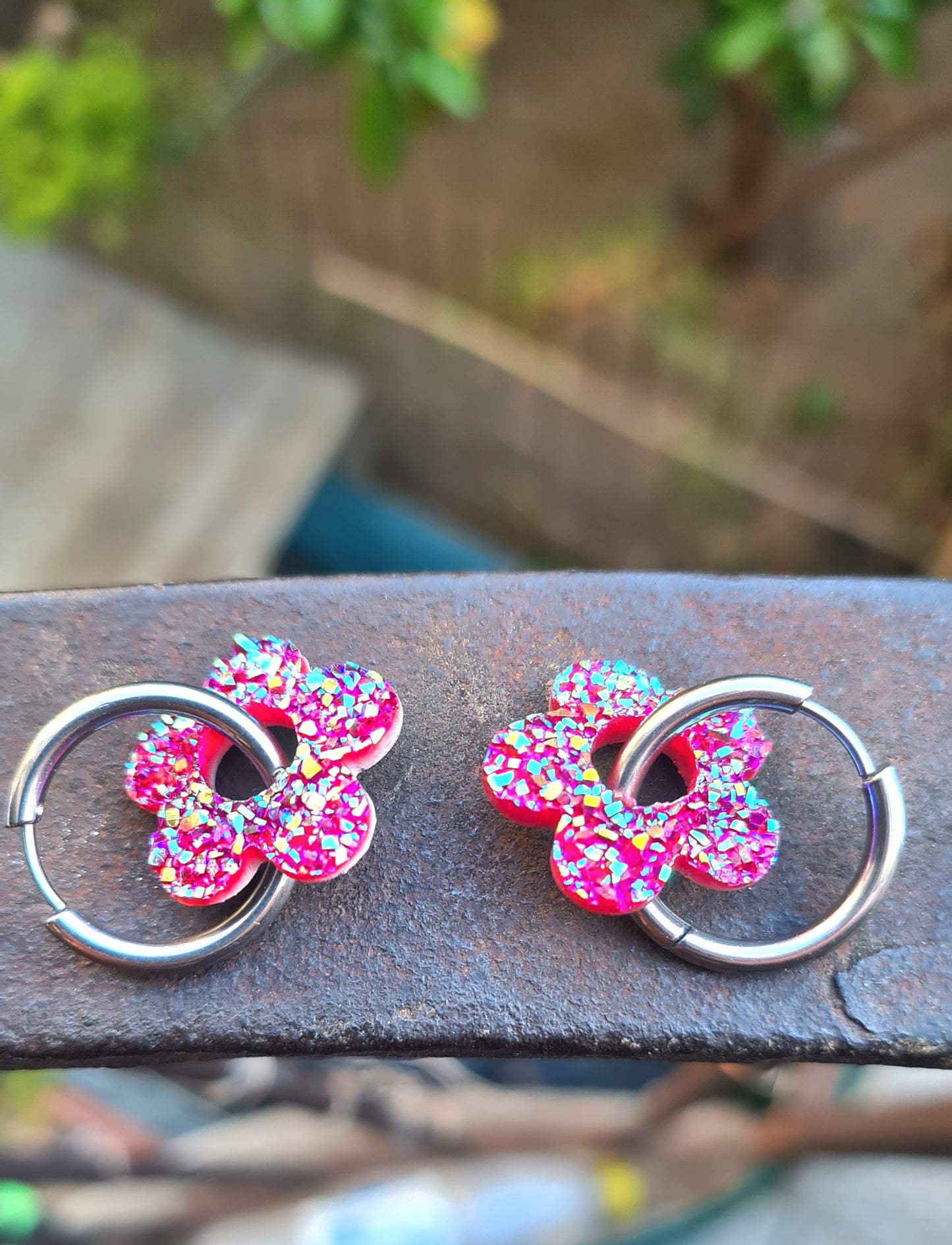 Aros acero inoxidable plateados con Flor de Acrílico Brillante para mujer. Sobre baranda de hierro.
