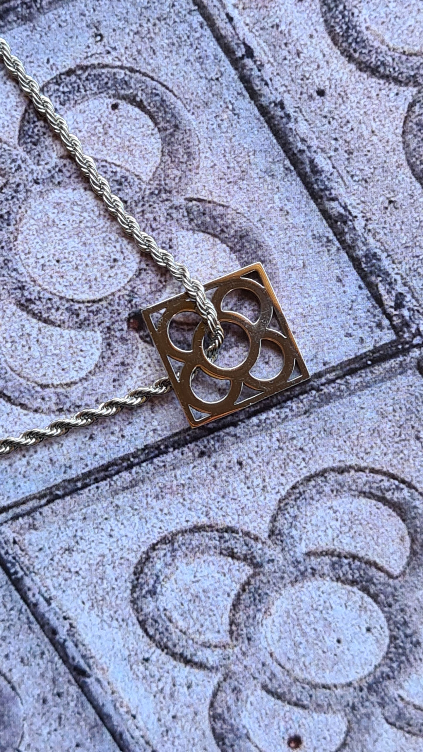 Colgante con la Flor de Barcelona de acero inoxidable cuadrada para mujer. Sobre baldosa Flor de Barcelona.