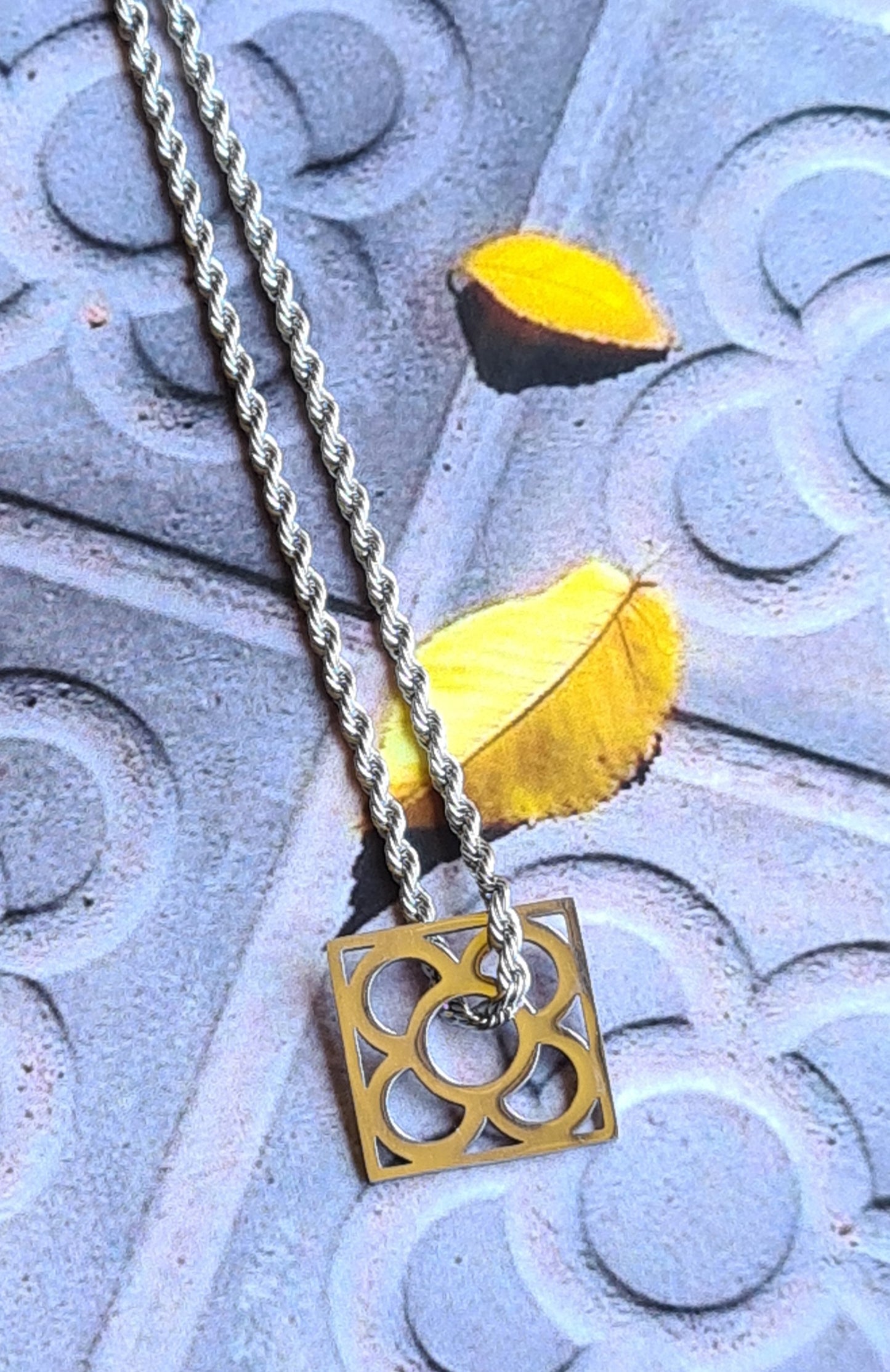 Colgante con la Flor de Barcelona de acero inoxidable cuadrada para mujer. Sobre baldosa Flor de Barcelona.