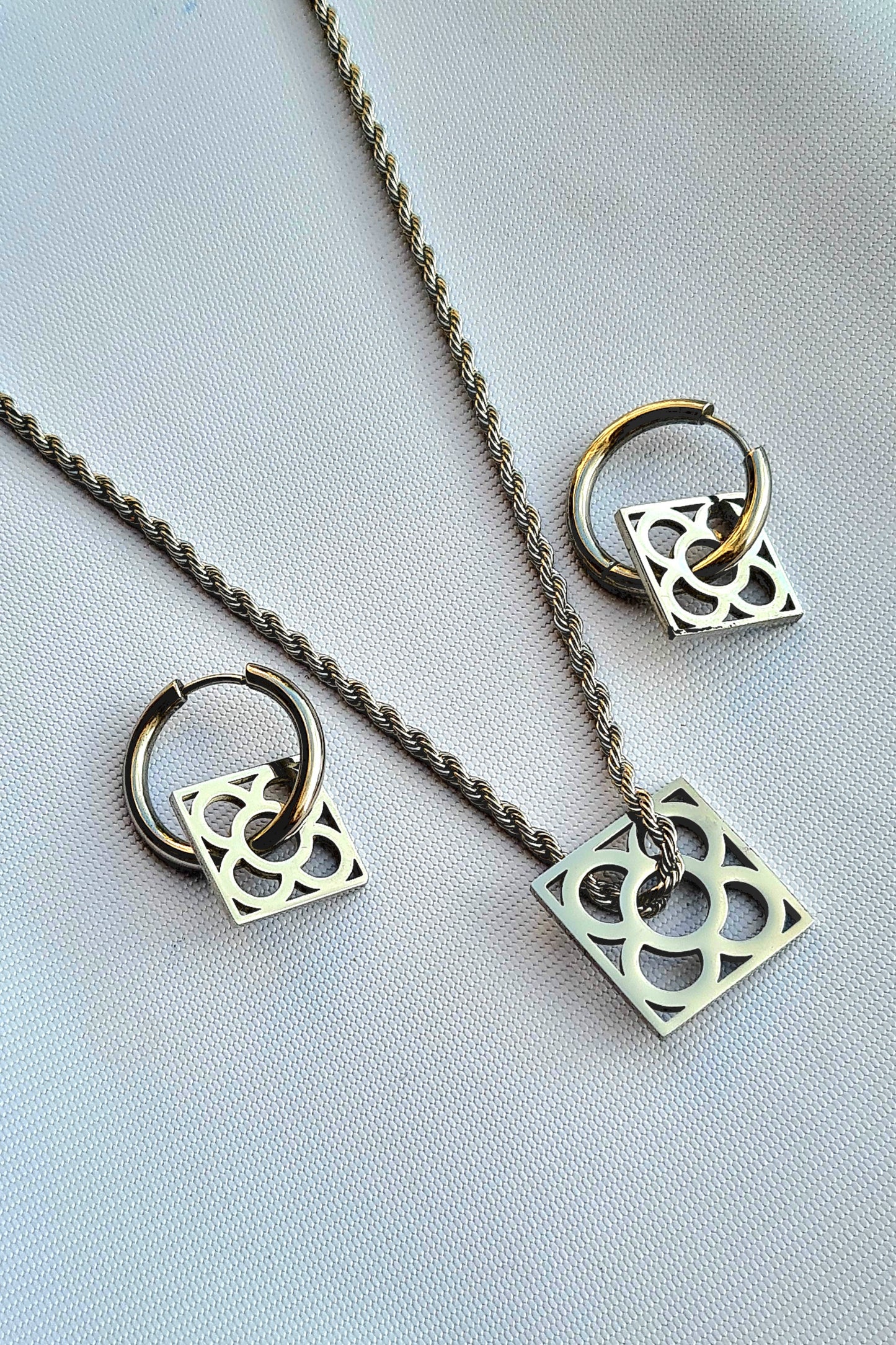 Conjunto con la Flor de Barcelona de acero inoxidable cuadrada para mujer. Fondo gris.