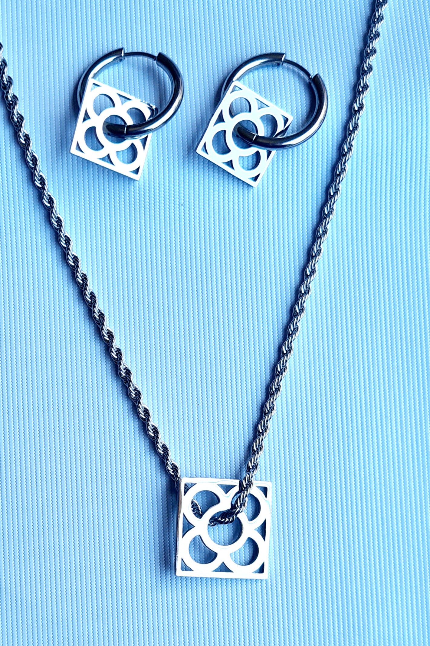 Conjunto con la Flor de Barcelona de acero inoxidable cuadrada para mujer. Fondo celeste.