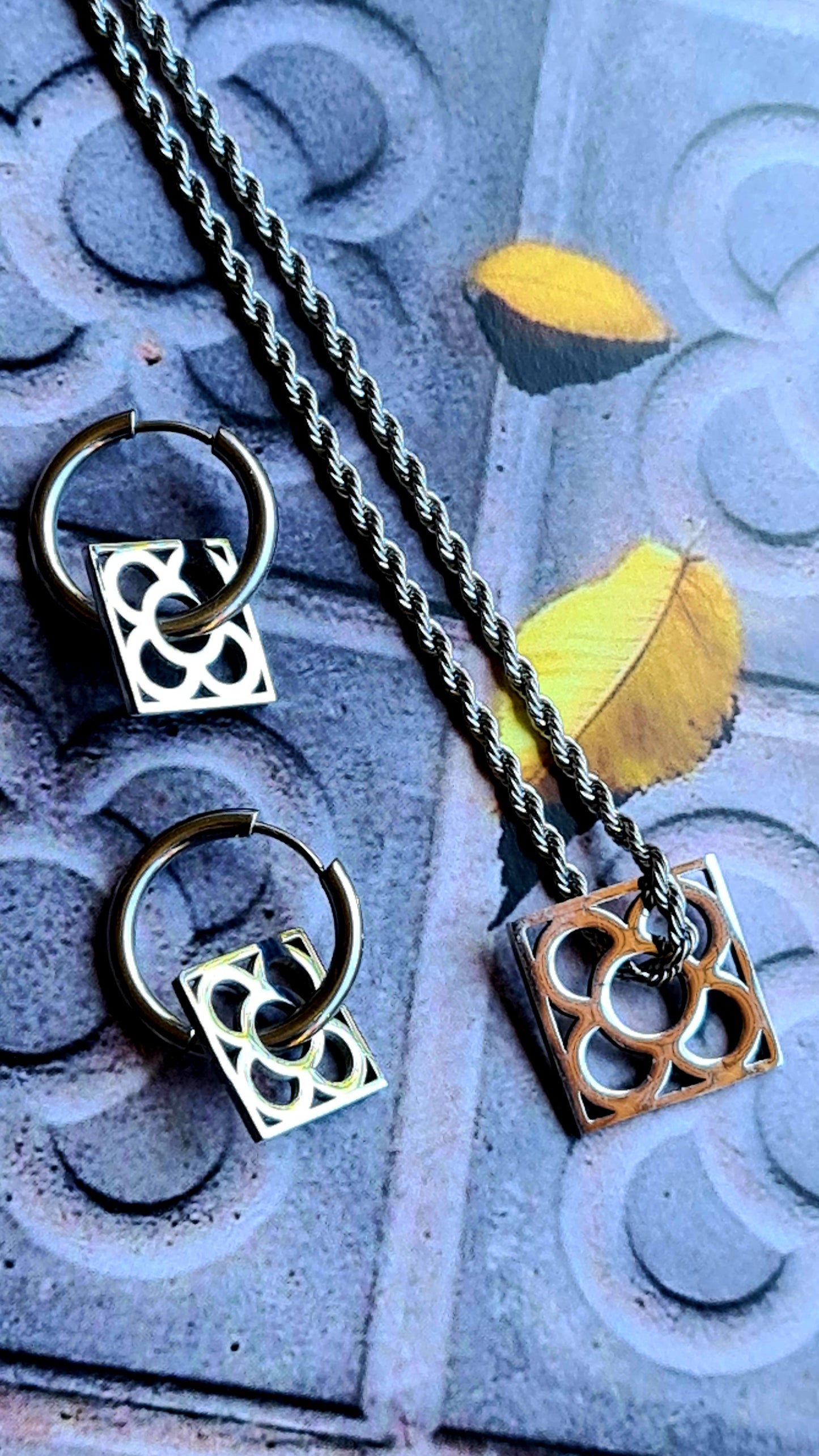 Conjunto con la Flor de Barcelona de acero inoxidable cuadrada para mujer. Sobre baldosa Flor de Barcelona.