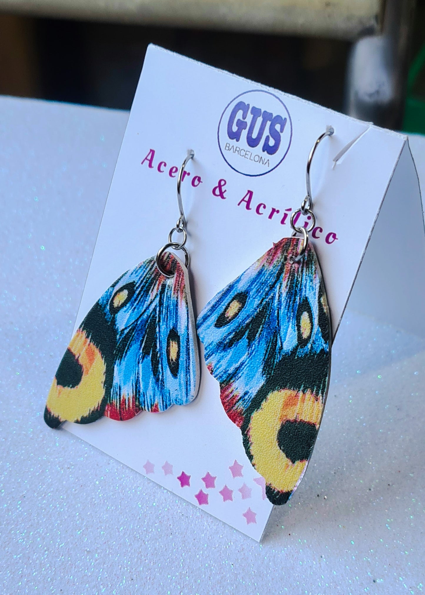 Pendientes Alas de Mariposa para mujer en Acero y Acrílico. Posa sobre cartón blanco.
