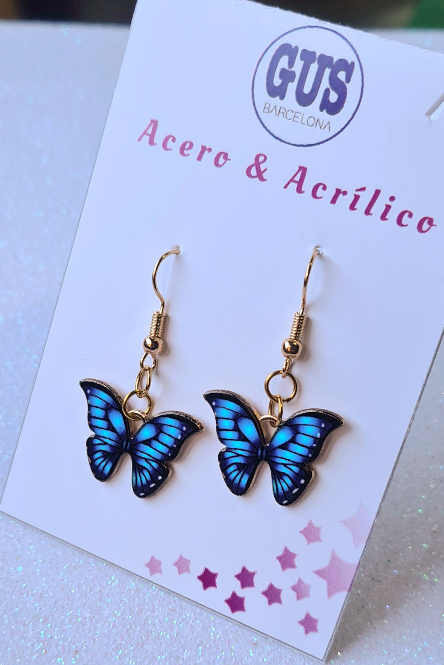 Pendientes Mariposa azul para mujer en Acero y Acrílico. Posa sobre cartón blanco.