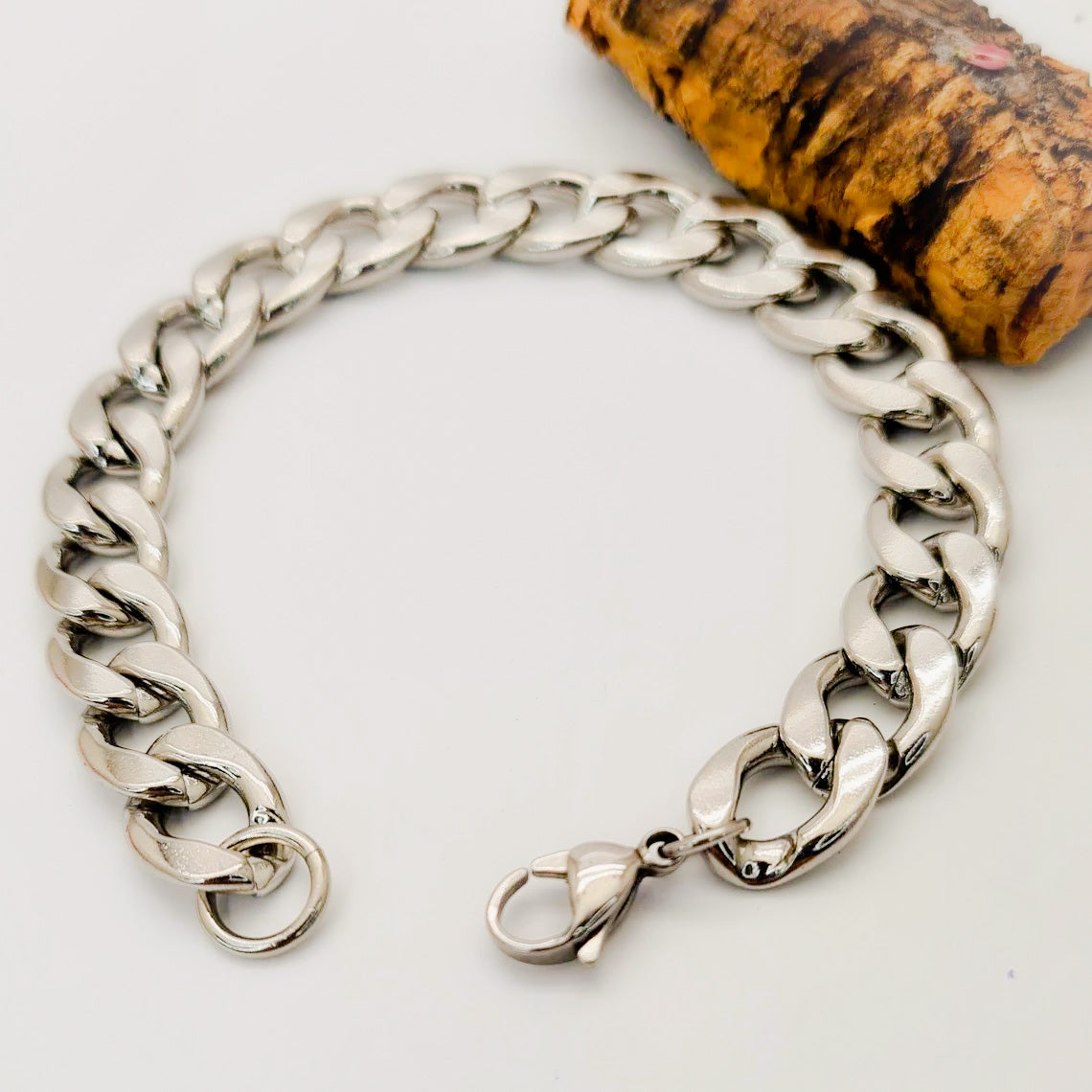 Pulsera acero inoxidable modelo Eslabón Grande, 12mm de ancho. Posa sobre fondo blanco con tronco.