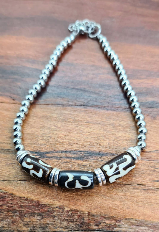 Pulsera unisex con tres piezas decoradas de hueso de yak, cadena de bolas y detalles plateados sobre fondo de madera.