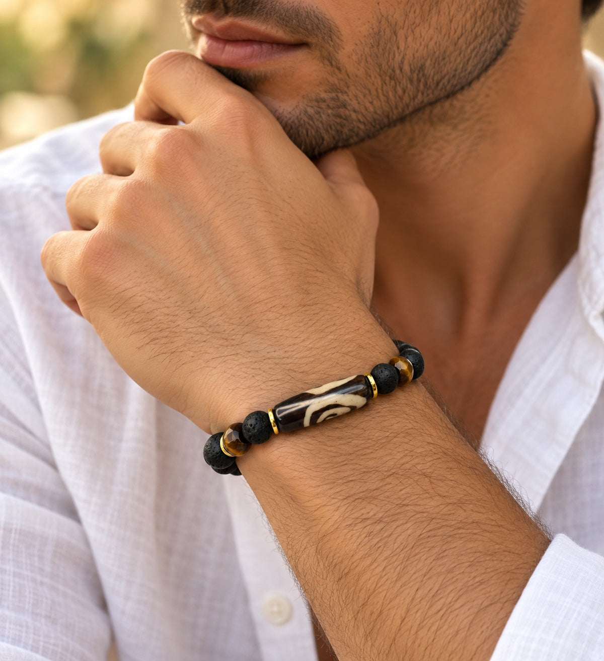 Pulsera artesanal negra de lava, hueso pintado y ojo de tigre puesta en muñeca masculina.