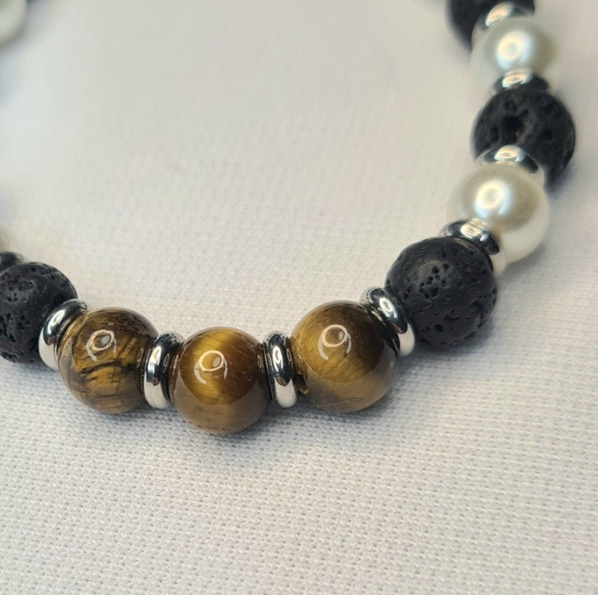 Detalle de pulsera con lava negra, ojo de tigre, cuentas de perla y separadores.
