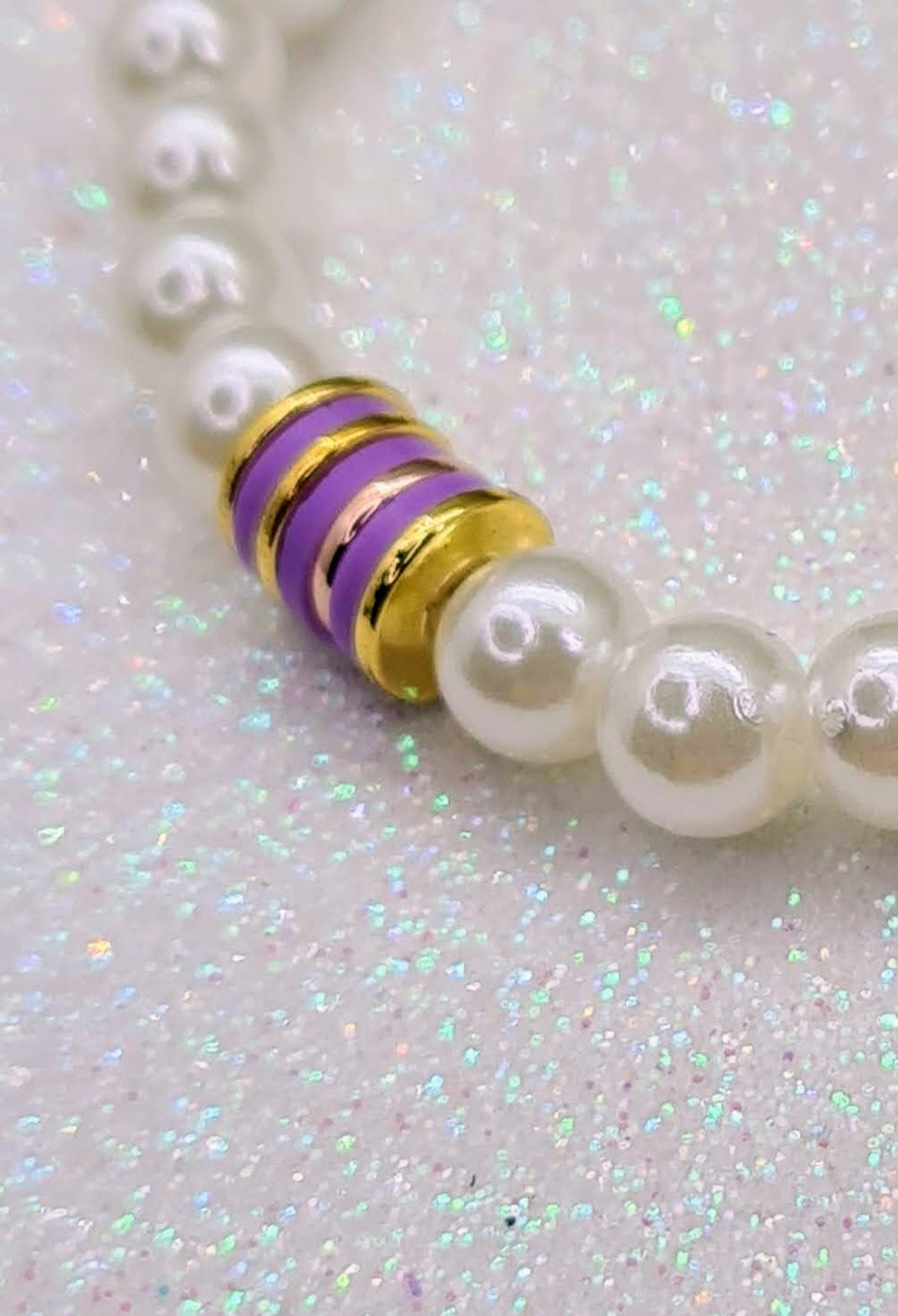 Detalle de pulsera de perlas blancas con discos de cerámica morados y detalles dorados.