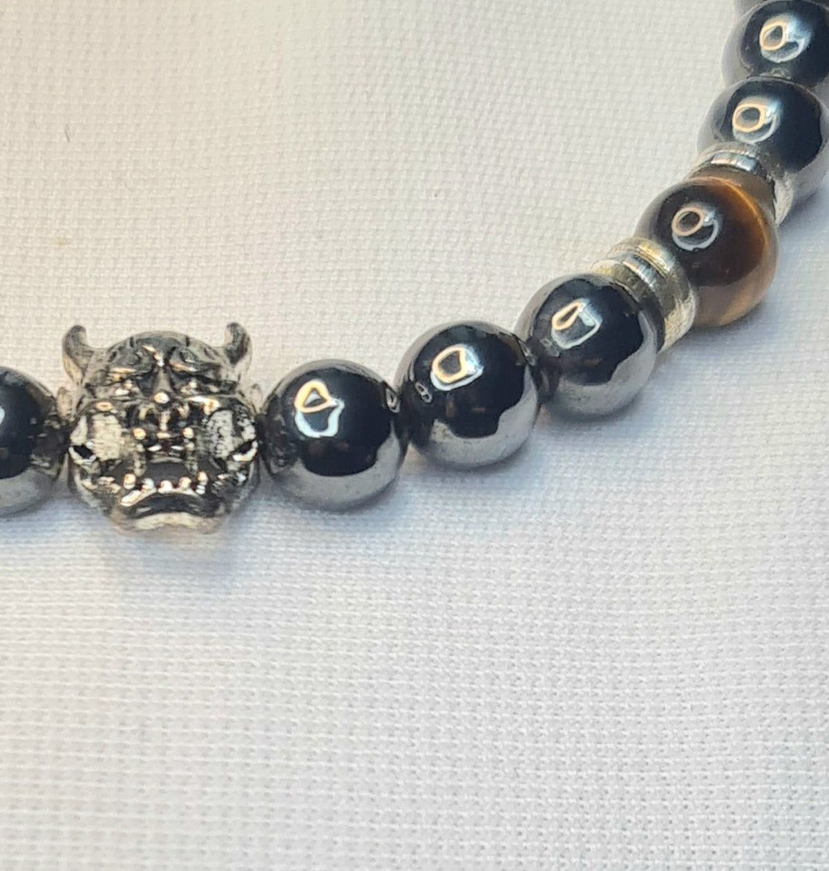 Detalle de cuentas de hematita, ojo de tigre y figura de demonio en pulsera masculina.