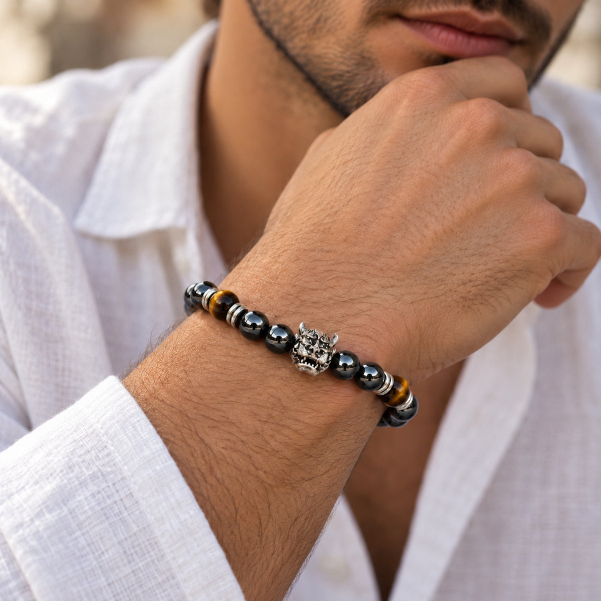 Hombre llevando pulsera de hematita facetada con ojo de tigre y figura central de demonio.