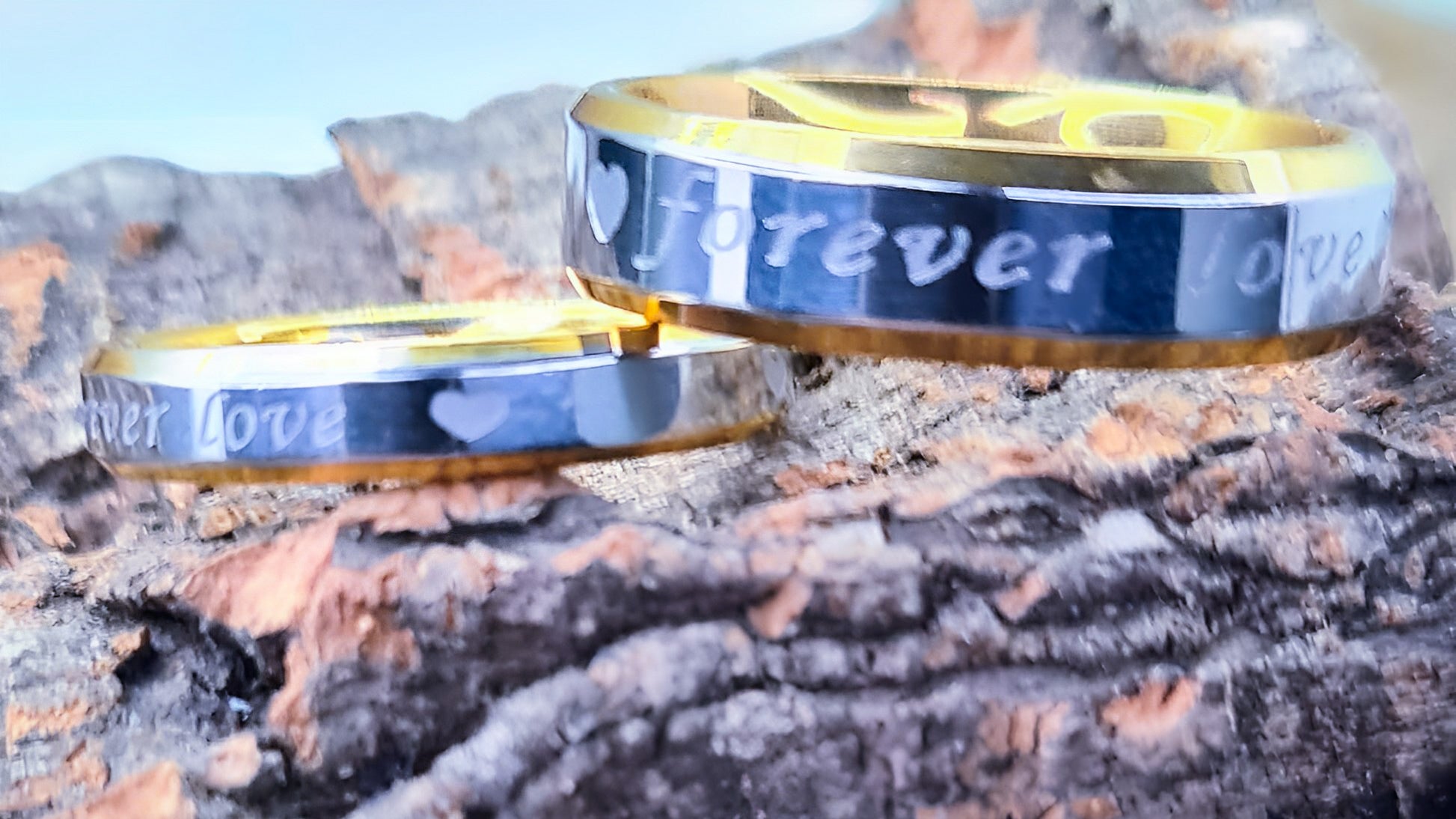 Anillos "Forever Love" tipo alianza de matrimonio o pareja en acero inoxidable bicolor y ancho de 4mm y 6mm. Se incluye grabado de nombres y fecha importante gratis. Posan sobre tronco de árbol.