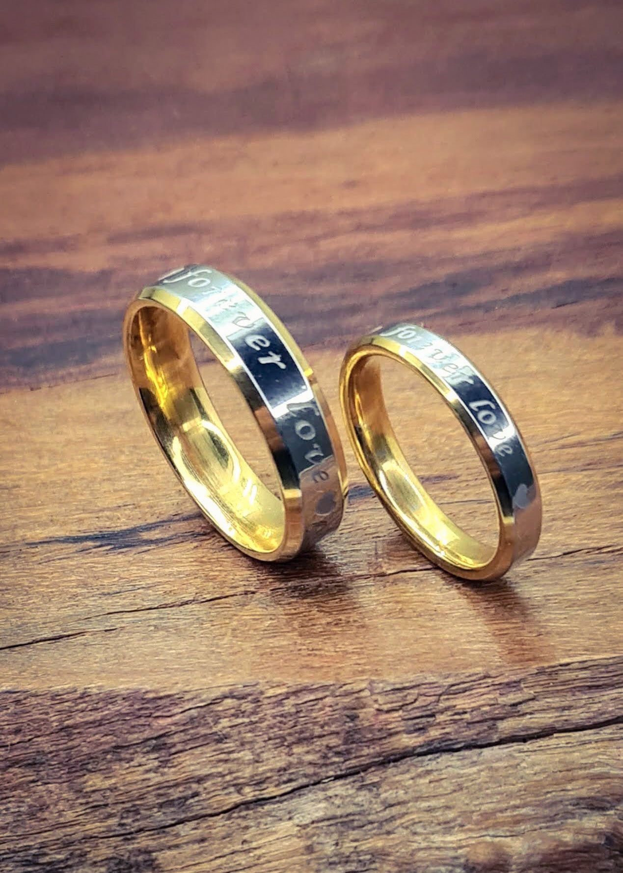 Anillos "Forever Love" tipo alianza de matrimonio o pareja en acero inoxidable bicolor y ancho de 4mm y 6mm. Se incluye grabado de nombres y fecha importante gratis. Posan sobre madera.