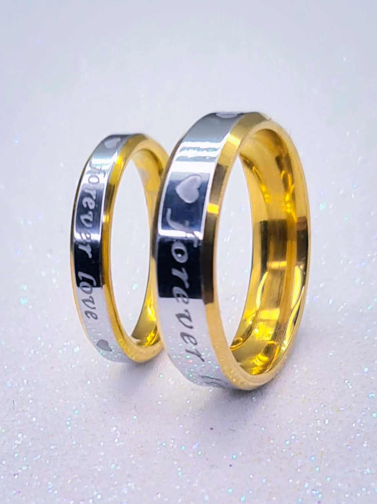 Anillos "Forever Love" tipo alianza de matrimonio o pareja en acero inoxidable bicolor y ancho de 4mm y 6mm. Se incluye grabado de nombres y fecha importante gratis. Posan sobre fondo blanco brillante.