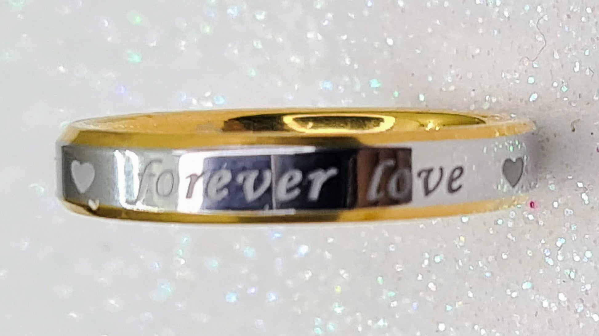 Vista frontal de alianza bicolor fina con corazones y frase "Forever Love".