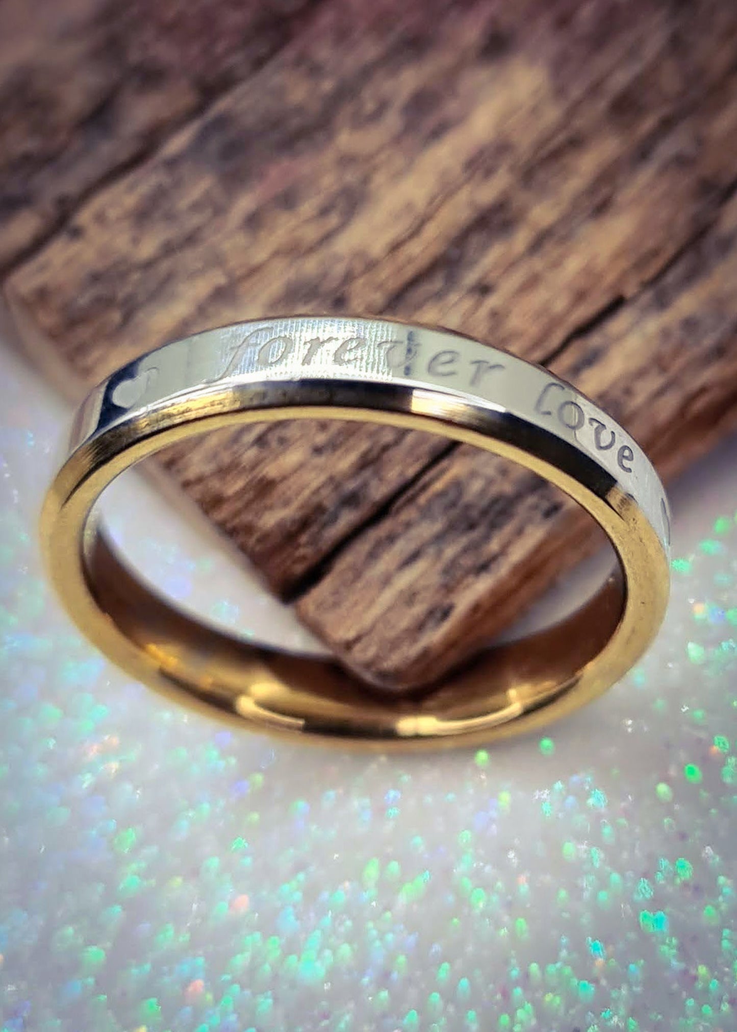 Anillo de pareja de acero inoxidable con inscripción "Forever Love" junto a una pieza de madera.