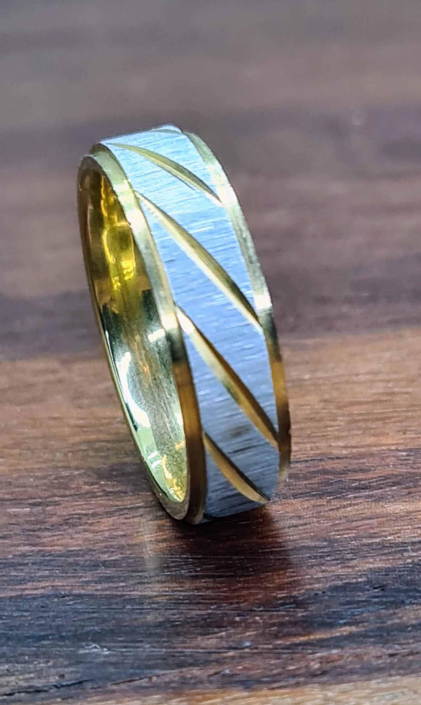 Anillo bicolor de 6 mm con líneas diagonales sobre superficie de madera.
