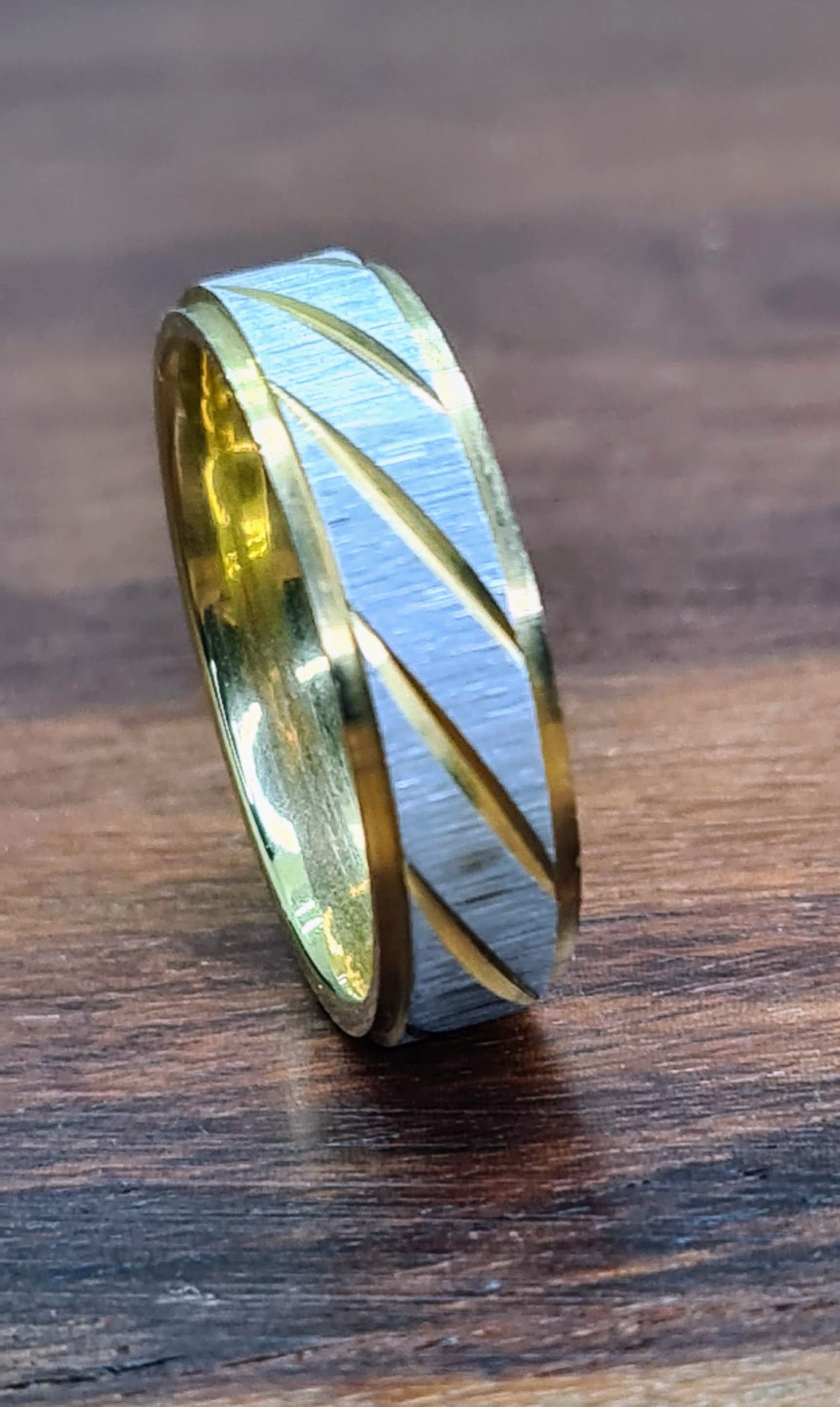 Anillo bicolor de 6 mm con líneas diagonales sobre superficie de madera.