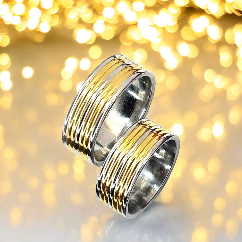 Dos Anillos tipo alianza de matrimonio o pareja en acero inoxidable bicolor y ancho de 8mm. Se incluye grabado de nombres y fecha importante gratis. Posan sobre fondo dorado.