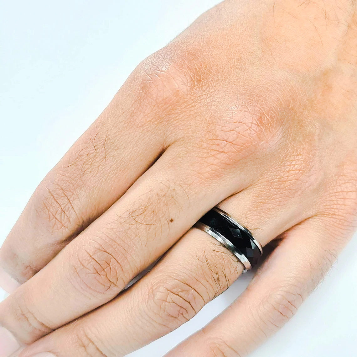Anillo tipo alianza de matrimonio o pareja en acero inoxidable bicolor negro y ancho de 8mm. Se incluye grabado de nombres y fecha importante gratis. Posa sobre mano de hombre.