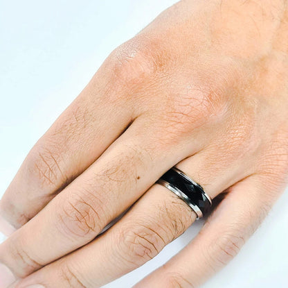 Anillo tipo alianza de matrimonio o pareja en acero inoxidable bicolor negro y ancho de 8mm. Se incluye grabado de nombres y fecha importante gratis. Posa sobre mano de hombre.