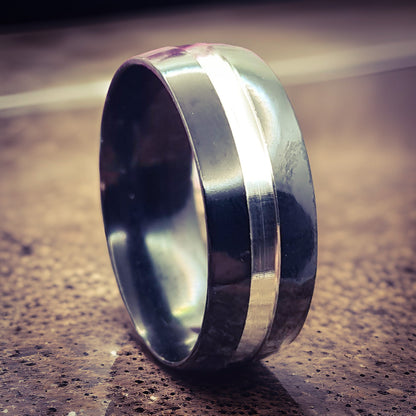Anillo tipo alianza de matrimonio o pareja en acero inoxidable bicolor negro y ancho de 8mm. Se incluye grabado de nombres y fecha importante gratis. Posa sobre mármol.