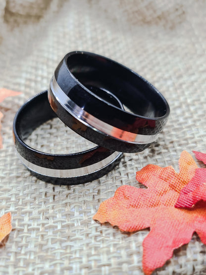 Dos Anillos tipo alianza de matrimonio o pareja en acero inoxidable bicolor negro y ancho de 8mm. Se incluye grabado de nombres y fecha importante gratis. Posan sobre saco.