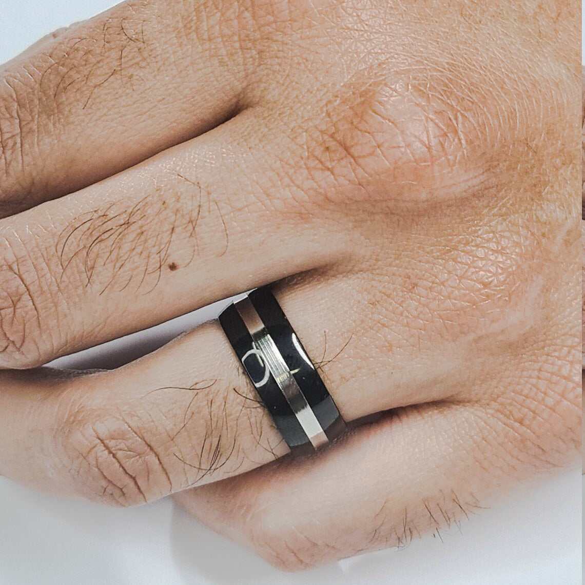 Anillo tipo alianza de matrimonio o pareja en acero inoxidable bicolor negro y ancho de 8mm. Se incluye grabado de nombres y fecha importante gratis. Posa sobre mano de hombre.