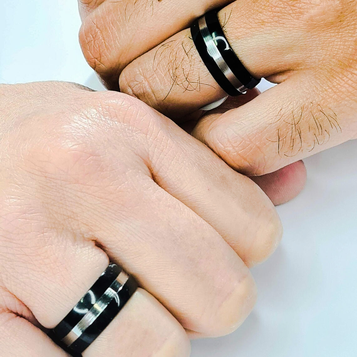 Dos Anillos tipo alianza de matrimonio o pareja en acero inoxidable bicolor negro y ancho de 8mm. Se incluye grabado de nombres y fecha importante gratis. Posan sobre mano de pareja.