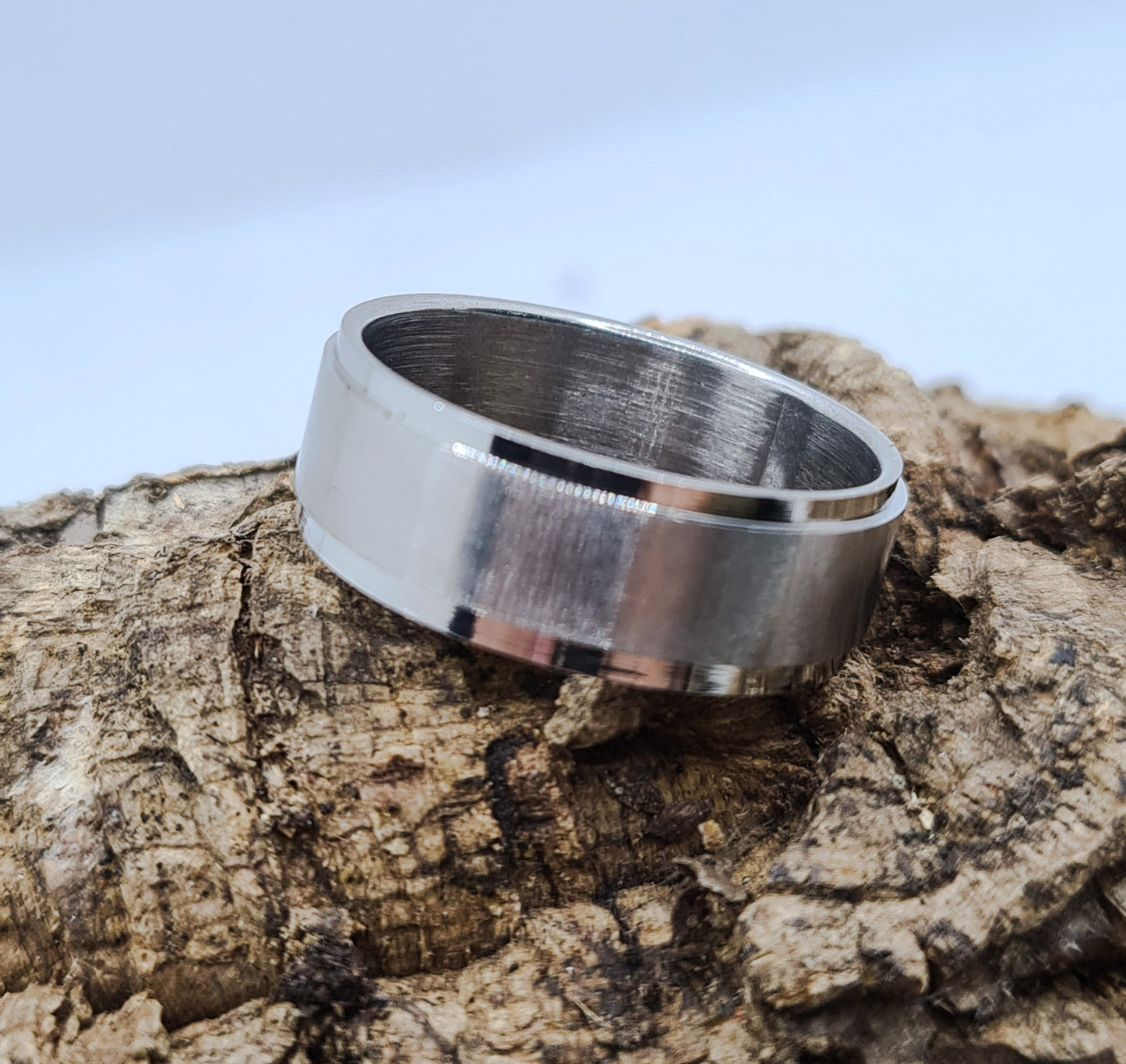 Anillo tipo alianza de matrimonio o pareja en acero inoxidable biselado y ancho de 8mm. Se incluye grabado de nombres y fecha importante gratis. Posa sobre tronco.
