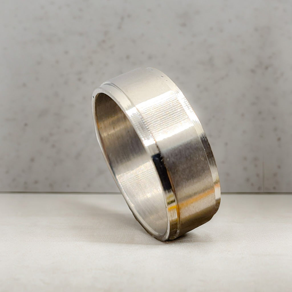 Anillo tipo alianza de matrimonio o pareja en acero inoxidable biselado y ancho de 8mm. Se incluye grabado de nombres y fecha importante gratis. Posa sobre mesa cocina.