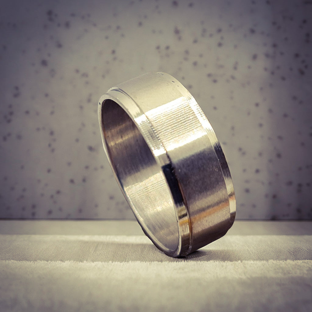 Anillo tipo alianza de matrimonio o pareja en acero inoxidable biselado y ancho de 8mm. Se incluye grabado de nombres y fecha importante gratis. Posa sobre mesa cocina.