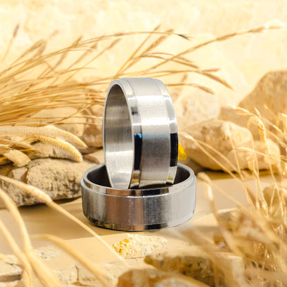 Dos Anillos tipo alianza de matrimonio o pareja en acero inoxidable biselado y ancho de 8mm. Se incluye grabado de nombres y fecha importante gratis. Posa sobre naturaleza.