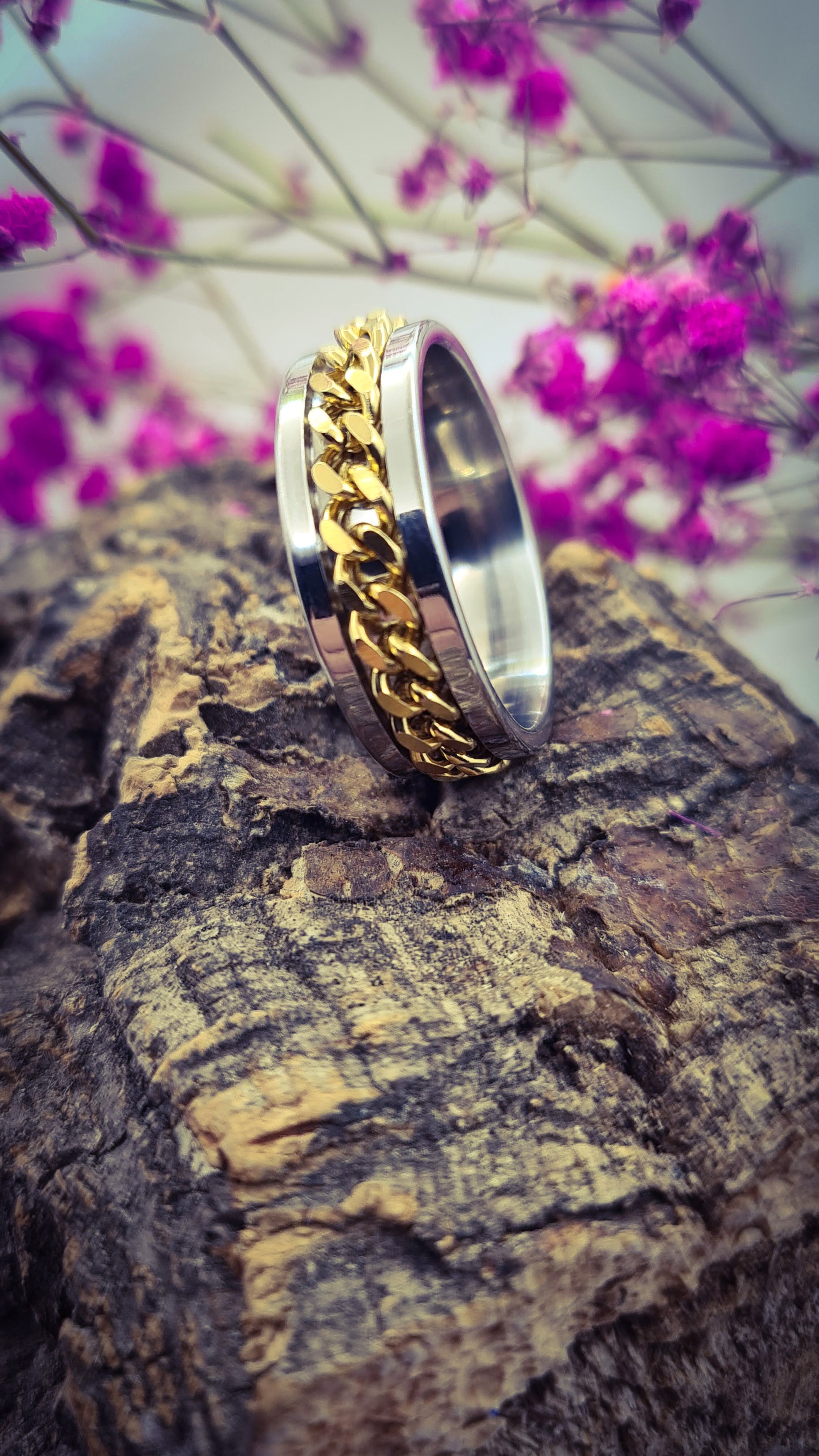 Anillo tipo alianza de matrimonio o pareja en acero inoxidable con cadena dorada y ancho de 8mm. Se incluye grabado de nombres y fecha importante gratis. Posa sobre tronco.