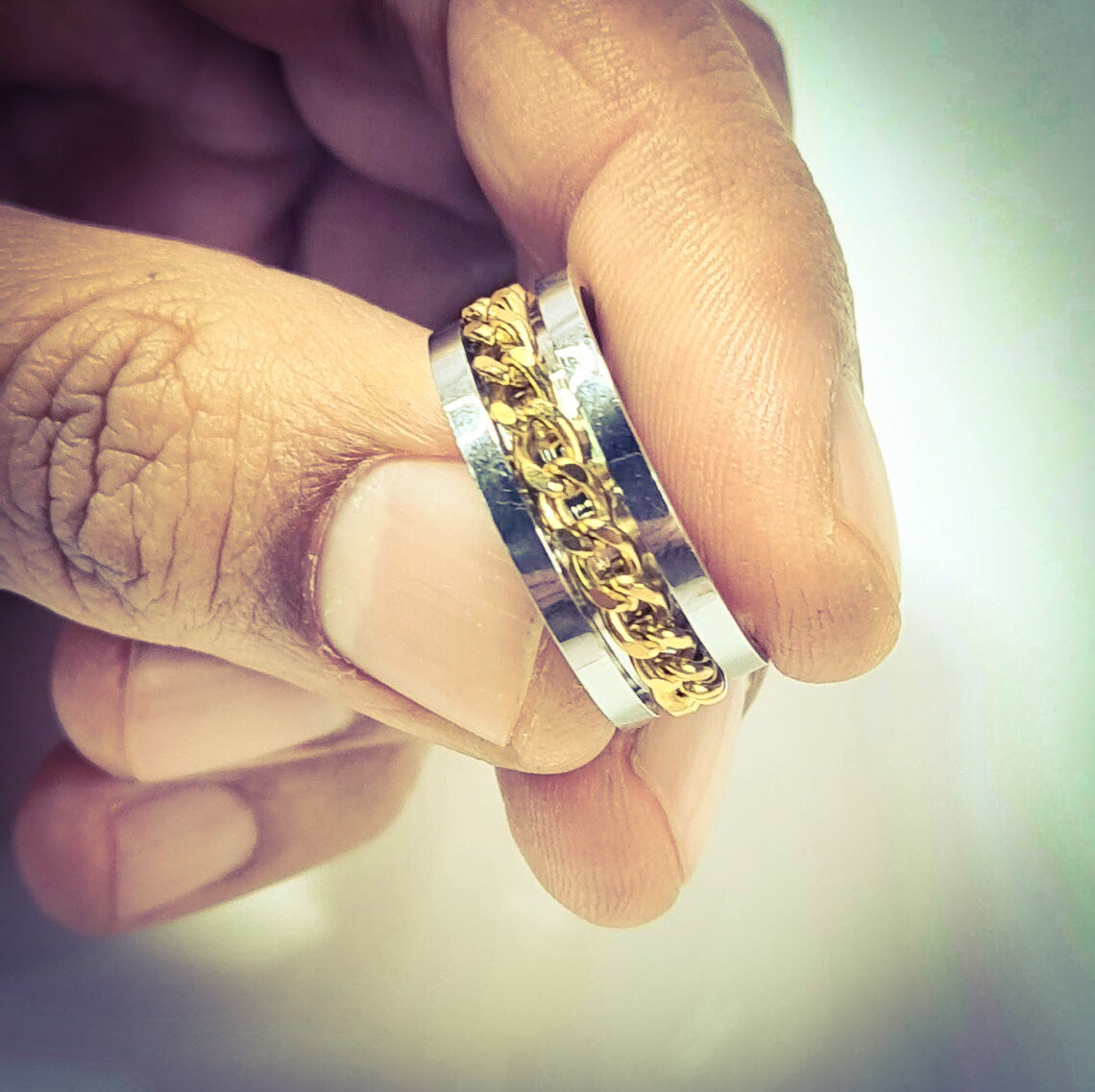Anillo tipo alianza de matrimonio o pareja en acero inoxidable con cadena dorada y ancho de 8mm. Se incluye grabado de nombres y fecha importante gratis. Posan sobre mano de hombre.