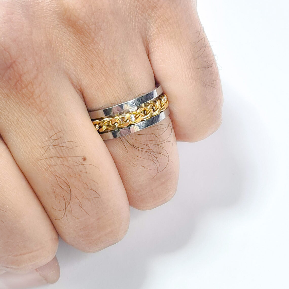 Anillo tipo alianza de matrimonio o pareja en acero inoxidable con cadena dorada y ancho de 8mm. Se incluye grabado de nombres y fecha importante gratis. Posan sobre mano de hombre.