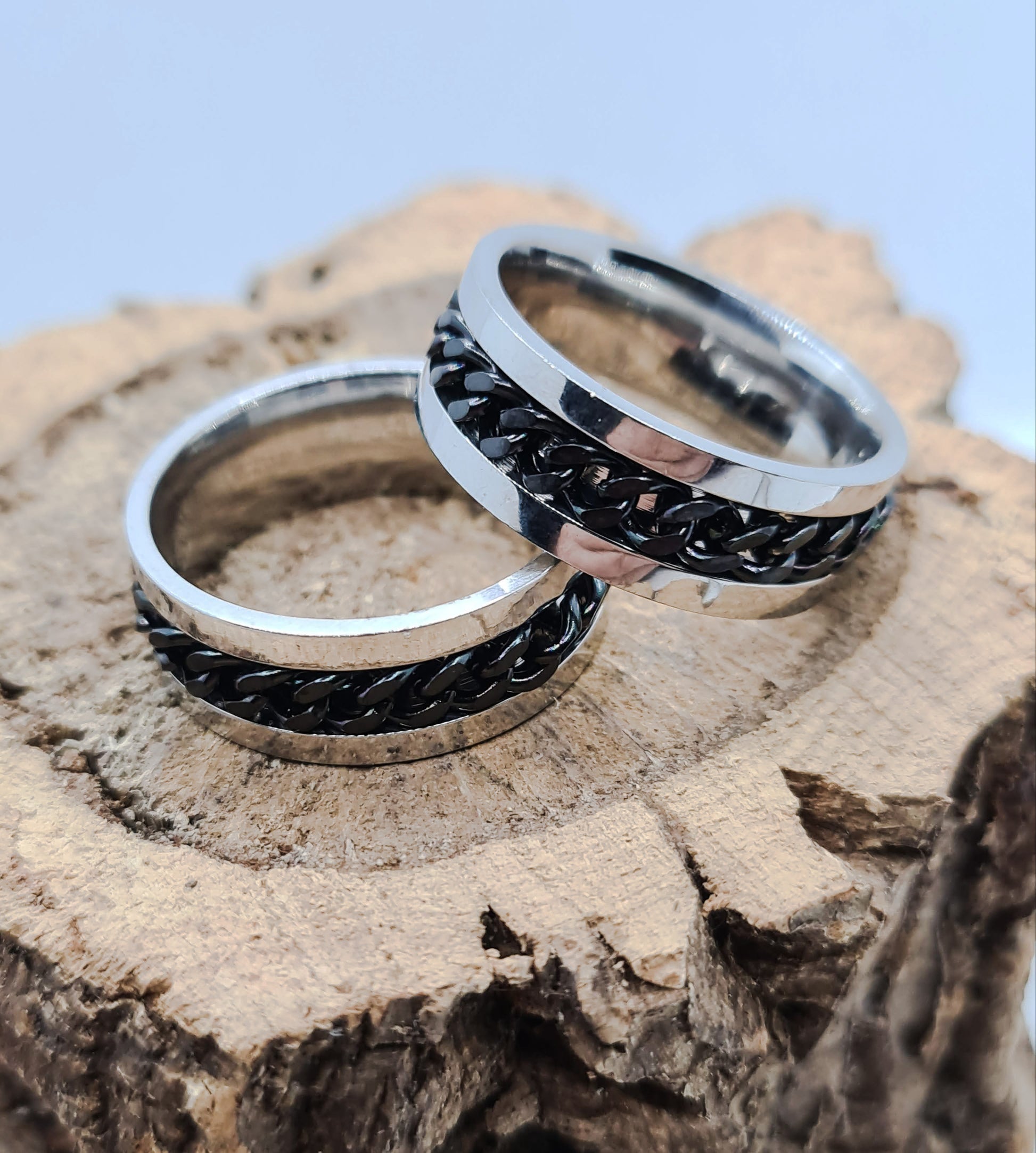 Dos Anillos tipo alianza de matrimonio o pareja en acero inoxidable con Cadena negra y ancho de 6mm. Se incluye grabado de nombres y fecha importante gratis. Posan sobre tronco.